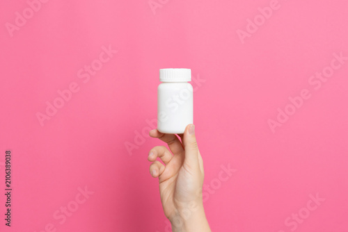 Hand holding white pill bottle on pink background