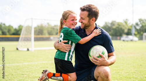 Father comforting young daughter after children’s soccer match during supportive family sports moment