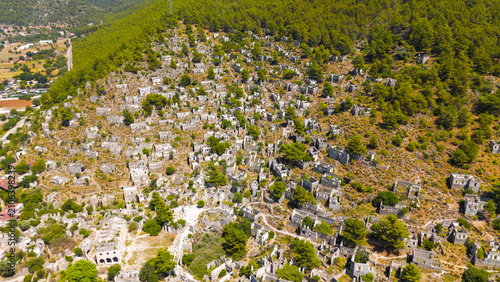 Kayakoy, Turkey. Wide aerial drone shot of abandoned ghost town showing Upper Church and stone house ruins sprawling across mountain slopes.. Aerial View