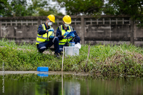 Environmental scientists or ecologists collecting water samples from a polluted canal for laboratory analysis and water quality monitoring to ensure industrial compliance and sustainability.