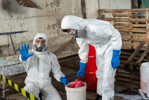Hazmat response team worker in protective suit making a stop hand gesture to a danger zone during a toxic chemical spill cleanup to ensure industrial safety and prevent hazardous accidents.