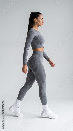 Fit athletic young woman in gray sportswear posing in studio