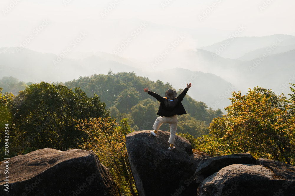Fototapeta premium Person stands atop rugged boulders, arms wide open