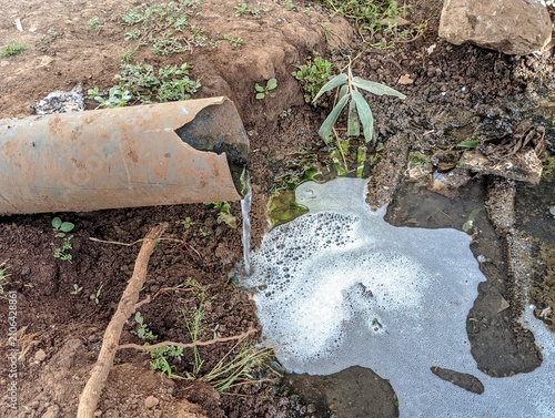 Industrial wastewater flowing from a rusty metal pipe into the soil causing environmental damage.