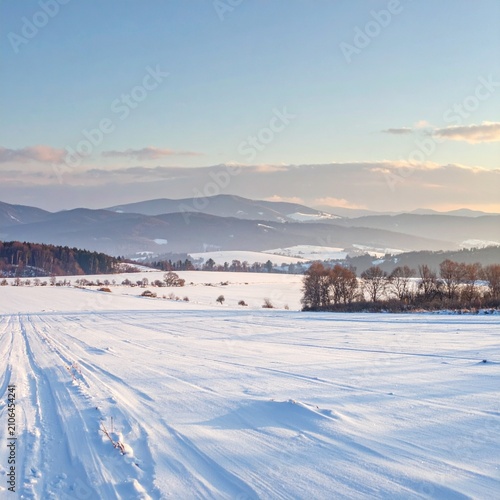 Snow Covered Field with Tracks and Distant Hills at Sunrise