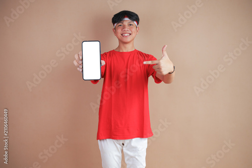 Smiling Indonesian Youth in Red T-shirt Holding and Pointing to Blank white Smartphone Screen