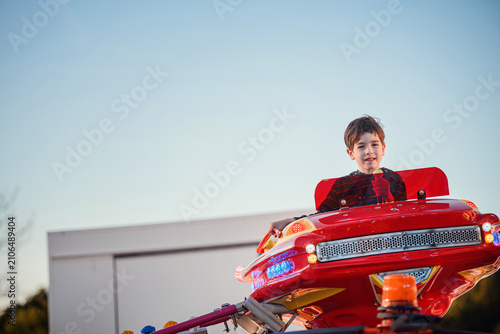 High perspective boy in red flying car smiles at camera above buildings dusk blue sky