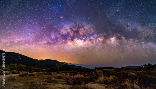 Milky Way arches over a serene valley landscape under a starry night sky, illuminated by a soft, orange glow