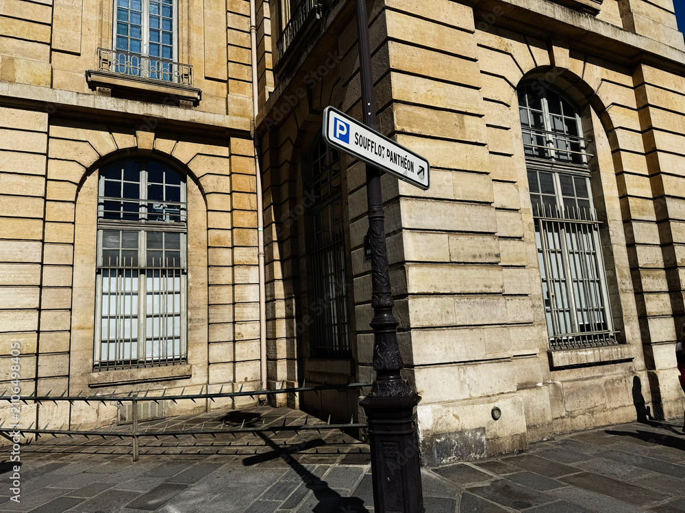 Fototapeta premium Historic Paris France street corner with sandstone building, arched windows and Soufflot Panthéon parking sign in warm sunlight