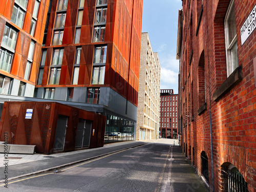 Modern red brick and corten steel architecture along a narrow street in Manchester UK with dramatic light and urban perspective