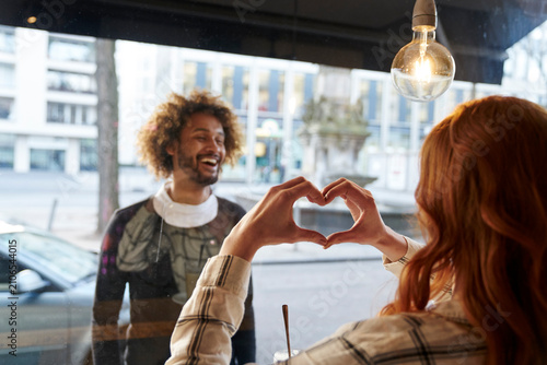 Woman shaping heart with her hands for man behind windowpane