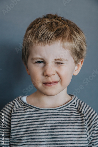 Playful boy winking against gray background