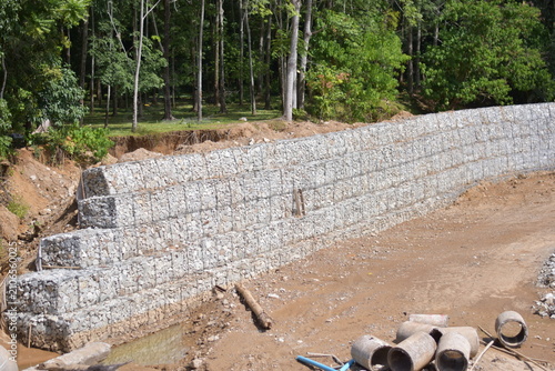 Retaining wall constructed from gabion baskets filled with stones viewed from the side outdoors, Gabion retaining wall