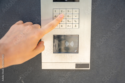 Person entering numbers on residential building intercom keypad. Secure access control enables visitor communication and controlled building entry