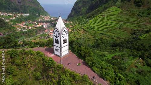 Sao Vicente Madeira Island, cinemetic drone of white chapel on hill aerial video flight past church to ocean coast to green mountain valley terraces. Portugal travel destination
