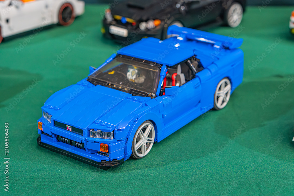 Fototapeta premium Summary Blue Lego sports car on green surface, contrasted by black wheels and white rims Silver roll bar, windshield, and silver-backdrop of additional cars - Kyiv, Ukraine - June 7, 2025