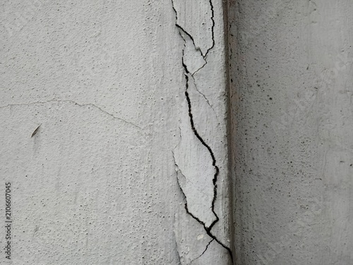 Close-up of a damaged concrete wall with a deep vertical crack and peeling paint.