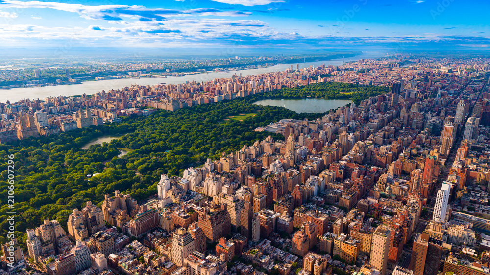 Obraz premium Central Park reservoir and surrounding Manhattan residential buildings. High angle view of large lake, green park trees, urban blocks, river, horizon under clouds.