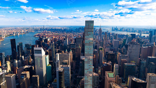 New York City skyline with 432 Park Avenue tower during the day. Aerial view of Manhattan skyscrapers, blue sky with white clouds, East River in the background.