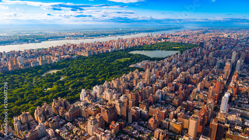 Central Park reservoir and surrounding Manhattan residential buildings. High angle view of large lake, green park trees, urban blocks, river, horizon under clouds.