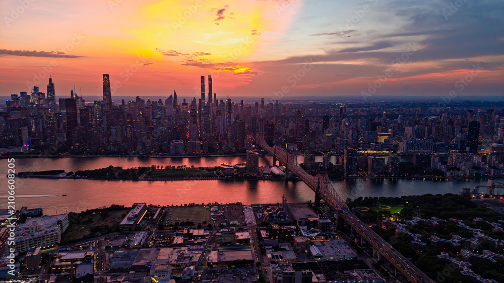 Obraz premium New York City skyline at sunset, view of Manhattan and Queensboro Bridge. Aerial view of the East River and skyscrapers under an orange sky.