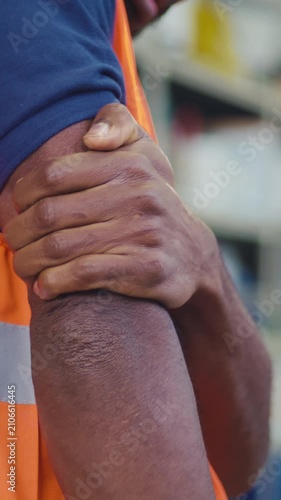 Worker in an orange safety vest experiencing upper arm pain, strain, fatigue, or injury caused by physical labor in workplace settings.