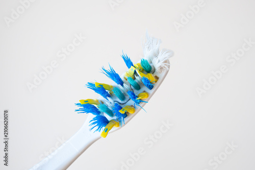 Close up of an old used toothbrush with frayed blue and yellow bristles isolated on a clean white background.