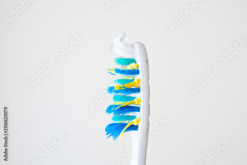 Close up of an old used toothbrush with frayed blue and yellow bristles isolated on a clean white background.
