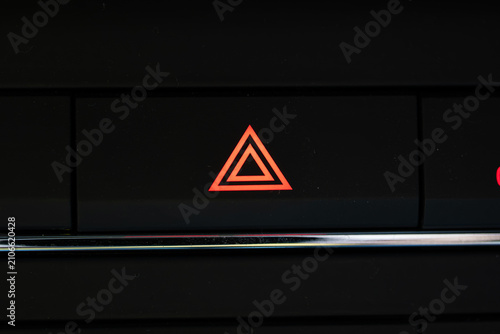 Close up of an illuminated red hazard warning light triangle button on a dark car interior dashboard console.