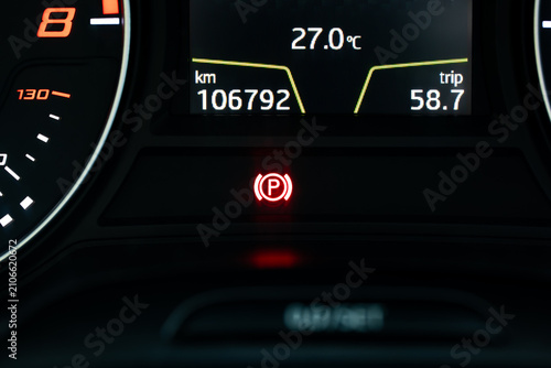 Close up of a car instrument cluster display showing mileage odometer, temperature, and illuminated red parking brake light.