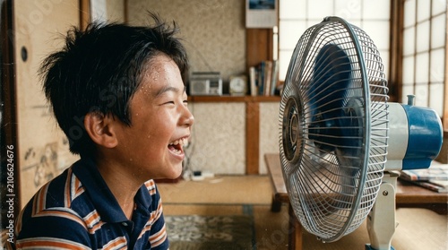 昭和の日本人小学生：和室の扇風機の前で大きな口を開けて風を浴び、楽しそうに涼む日本人小学生男子の夏休みクローズアップポートレート