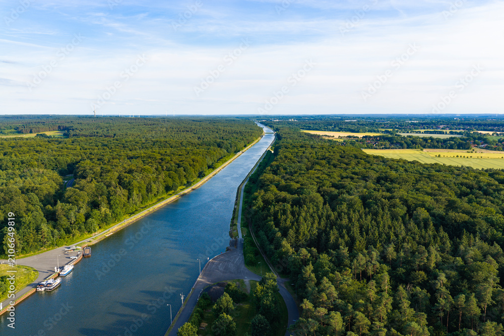 Obraz premium Cargo ship passing through canal in Germany. Transport logistics. Canal aerial view. Travel and logistics. Kiel canal aerial footage. Inland waterway