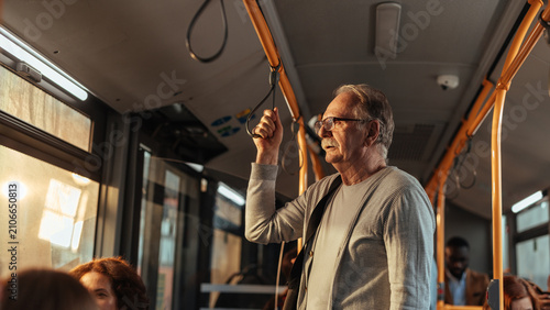 Senior man standing in bus using handrail