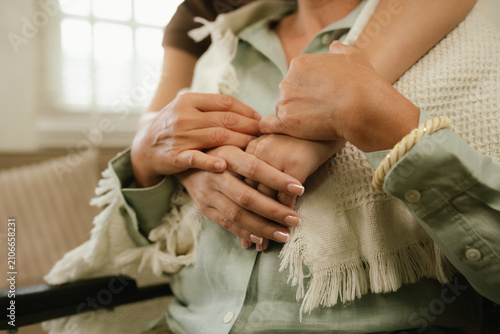 Young caregiver warmly hugging a smiling senior woman at home, expressing love, comfort, trust, and compassionate elderly care.