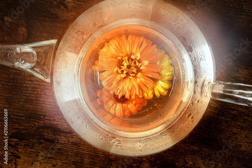 Fresh calendula herbal tea in a glass teapot, a flat lay