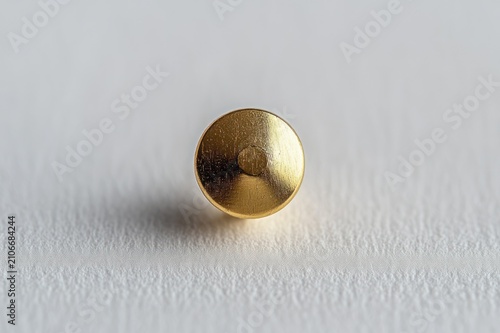Minimalist golden metal push pin head on textured white paper, close-up still life with soft shadow conveying calm focus and simplicity