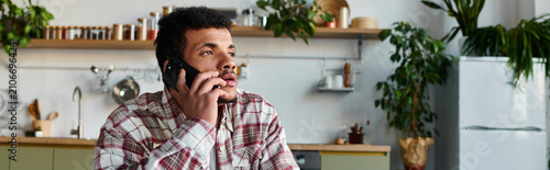 Canvastavla Handsome young man engages in a phone conversation while sitting in a bright kitchen