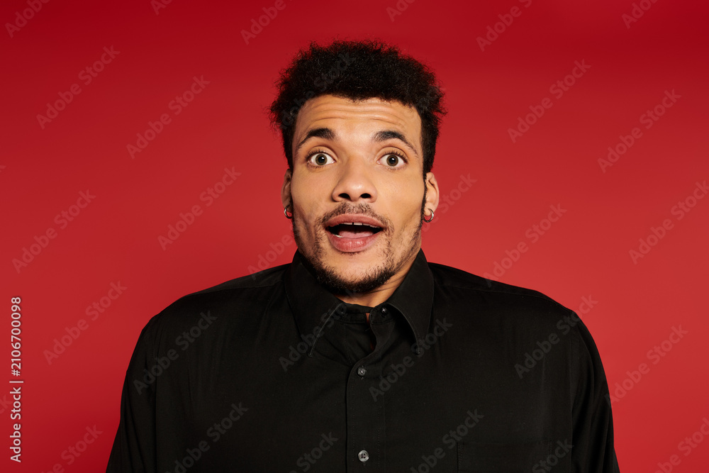 Obraz premium A young handsome man shows a surprised expression while posing against a bright red background.