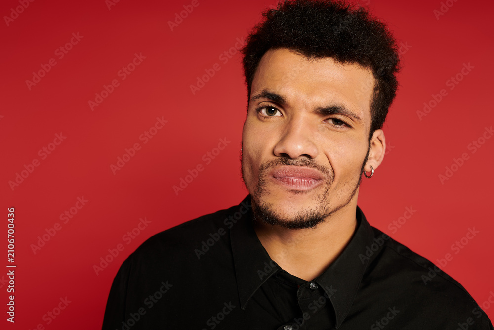 Obraz premium A young handsome man displays a playful expression against a vibrant red backdrop.