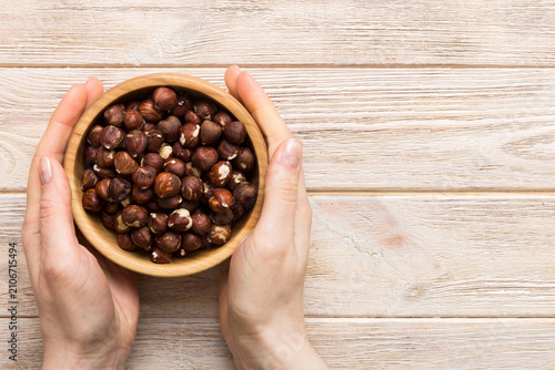 Woman hands holding a wooden bowl with hazelnut nuts. Healthy food and snack. Vegetarian snacks of different nuts