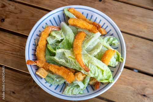 A bowl holds a mix of fresh lettuce, croutons, and crispy fried shrimp, ready to be enjoyed. This salad is perfect for lunch or dinner, adding flavor and texture to the meal.