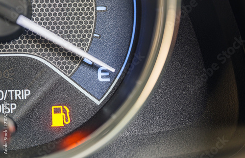Macro close-up of a car dashboard fuel gauge needle pointing to empty (E), with a fuel pump warning icon illuminated, Low Fuel Warning Light on car Dashboard Display