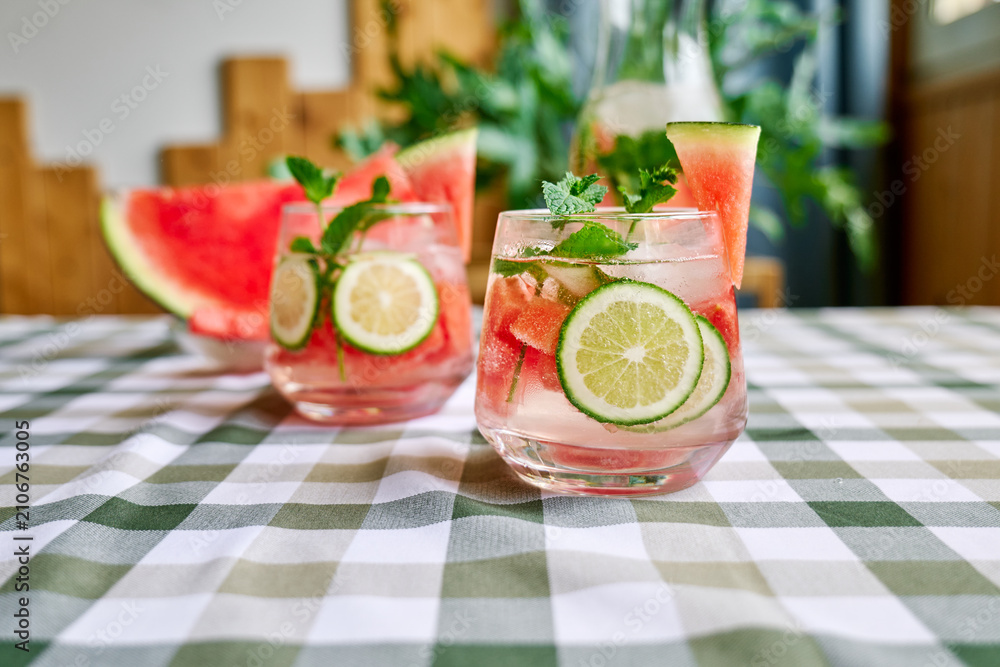 Obraz premium Summer refreshing watermelon drink with ice, mint and slices of lime on the table. Fresh healthy cold melon beverage. Fruit infused water, herbs and lemon.