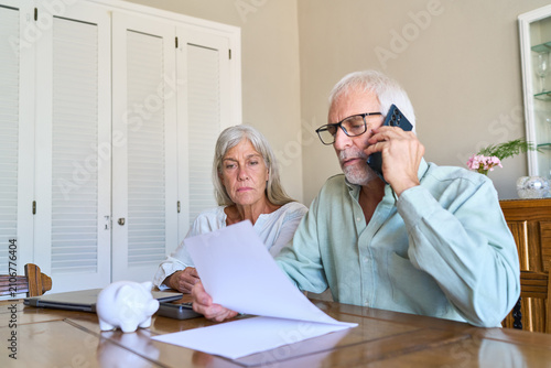 Retirement Planning And Financial Protection: Senior Couple Manages Finances, Reviews Documents, And Seeks Professional Advice On Phone