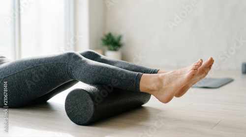 Severe knee pain relief concept. Person using a foam roller to stretch and massage leg muscles on a wooden floor indoors.