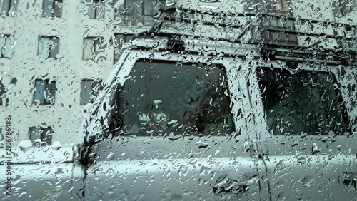 Foto A rain-lashed window obscures the background, showing a blurred, watery view of a white off-road vehicle parked in front of a residential building