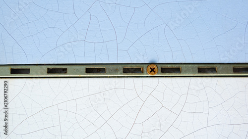 Rusty screw on metal track between blue and white cracked paint