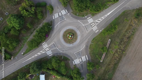 Aerial view of a roundabout in Dambach-La-Ville, France. A car drives through. The roundabout is surrounded by trees and grass, shot by a drone.