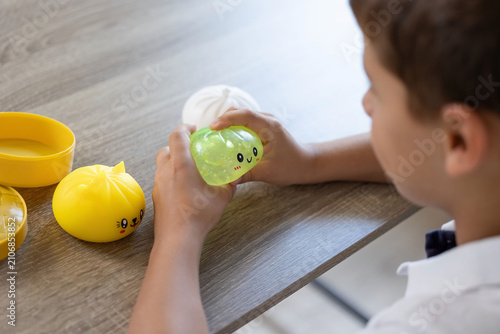 Fotografie Close view of child hands squeezing translucent green squishy toy while yellow t