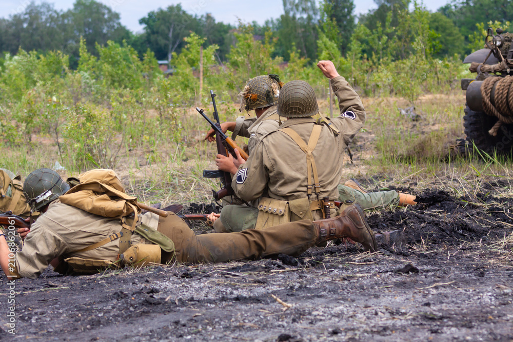Fototapeta premium Historical reenactment. Soldiers from a World War II infantry division on the battlefield. View from behind.